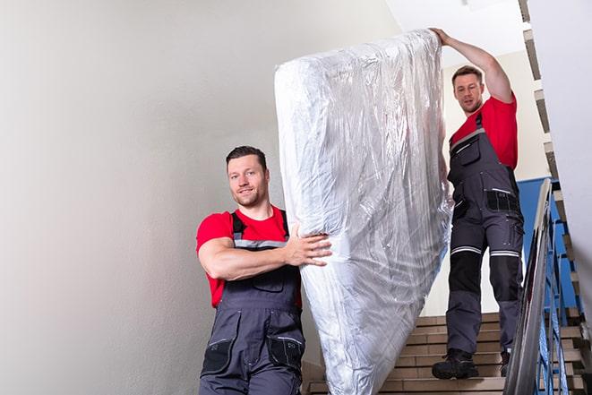 two workers hauling a box spring out of a building in Roxbury Crossing, MA